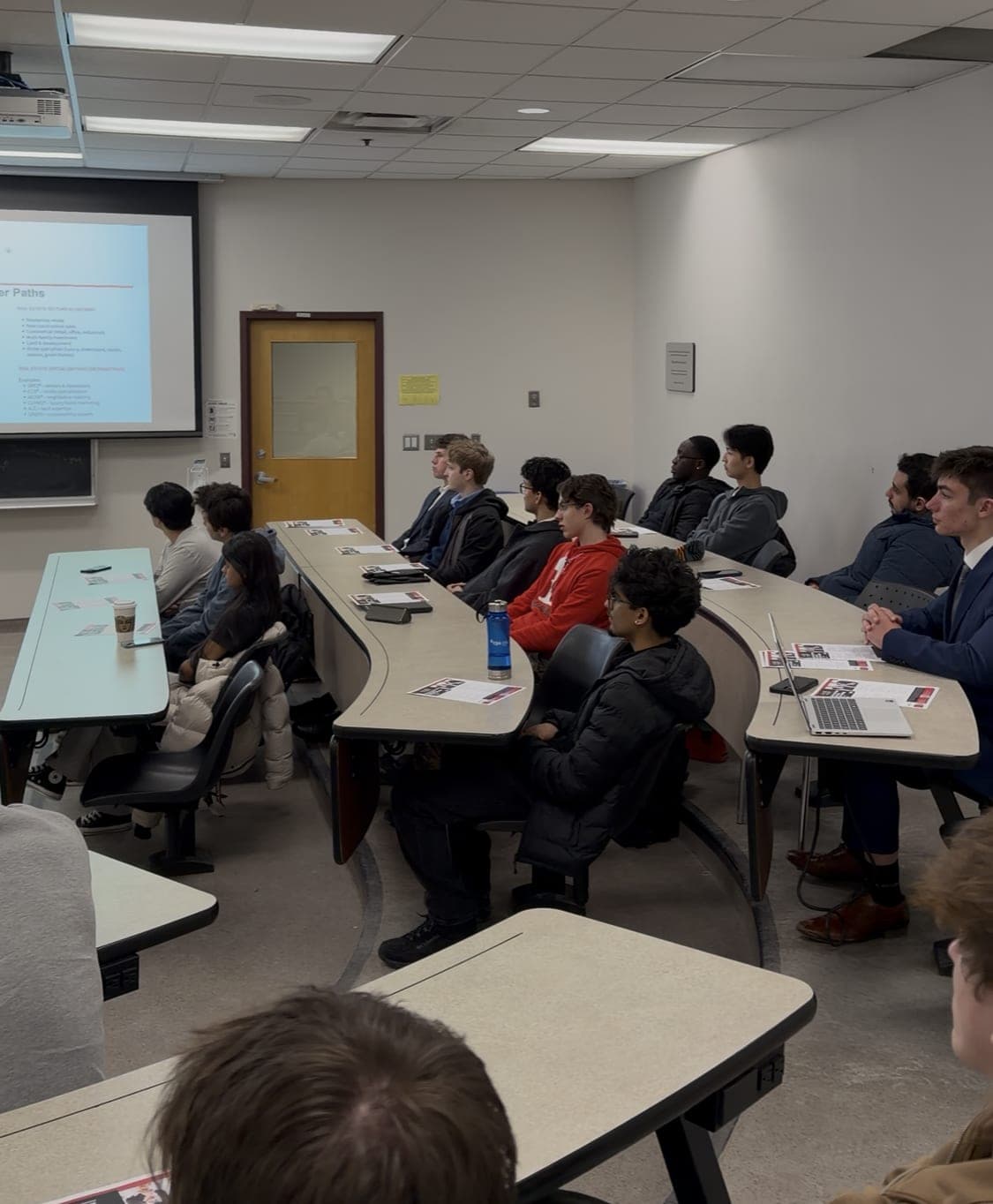 Students seated at curved desks in the lecture room, listening to the talk.