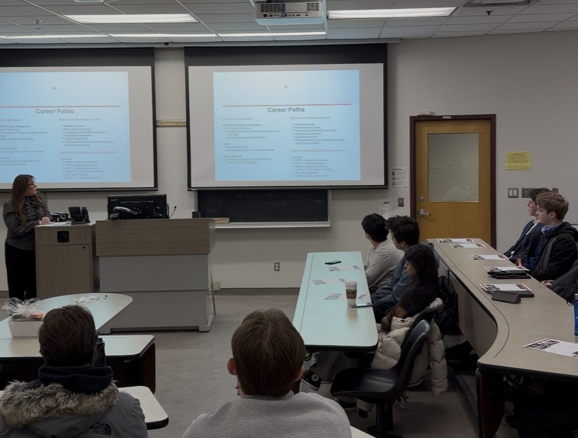 A wide view of the lecture room: Stacey Adamson presents on two screens while students listen from the curved rows.