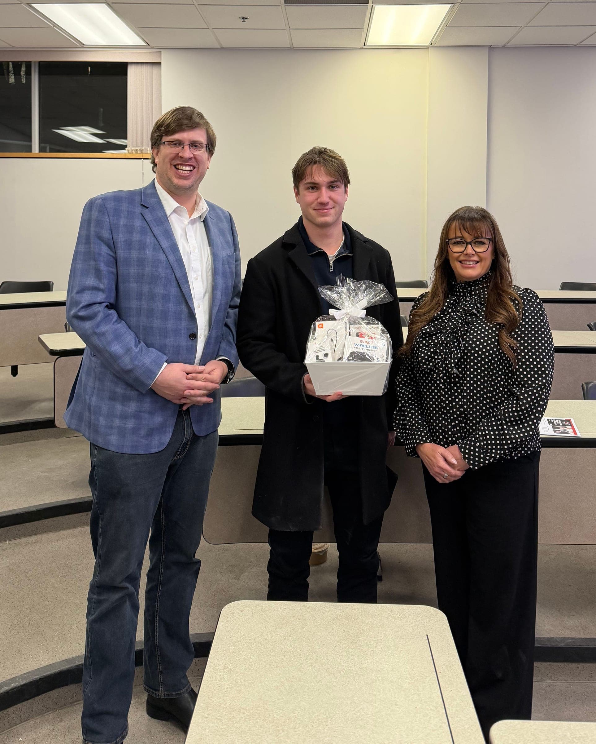Nic Von Bredow and Stacey Adamson stand with a student holding a gift basket.